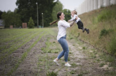 Fotografie einer jungen Frau, die ein kleines Kind liebevoll in die Luft hebt
