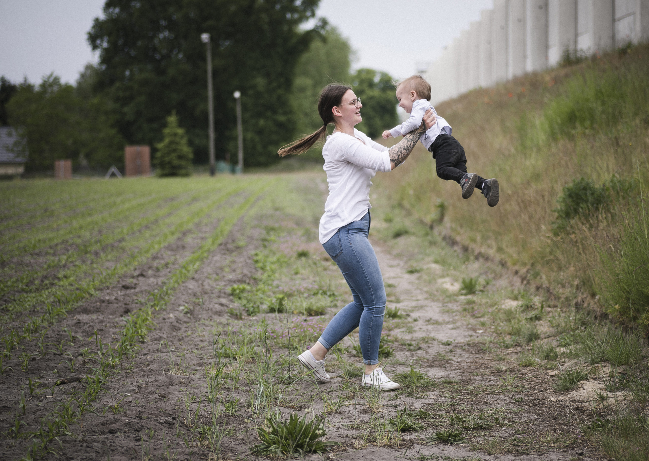 Fotografie einer jungen Frau, die ein kleines Kind liebevoll in die Luft hebt